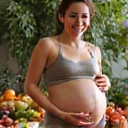 Femme enceinte souriante avec des fruits et légumes, symbolisant la nutrition pendant la grossesse